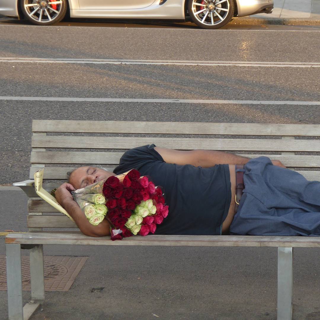 A flower salesman naps before starting his evening shift trying to sell roses to locals and tourists.